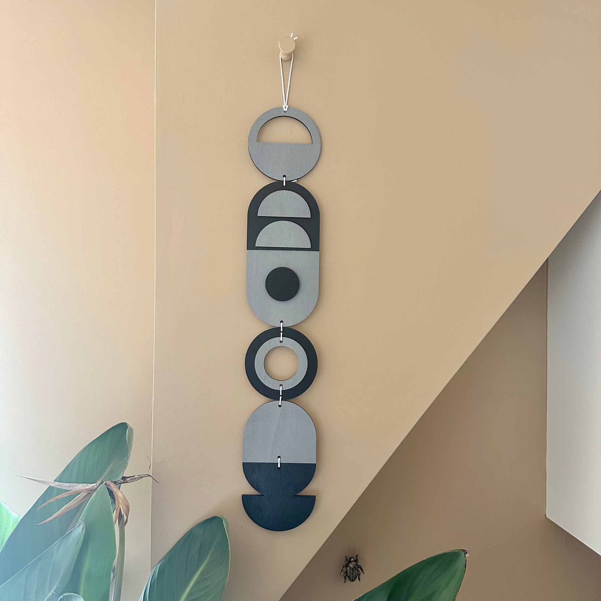 A black and grey handmade geometric wood wall hanging. In a modern Bauhaus art style. Featuring a textured effect through layer wood pieces and laser etching. Measuring 68cm in length x 10cm wide