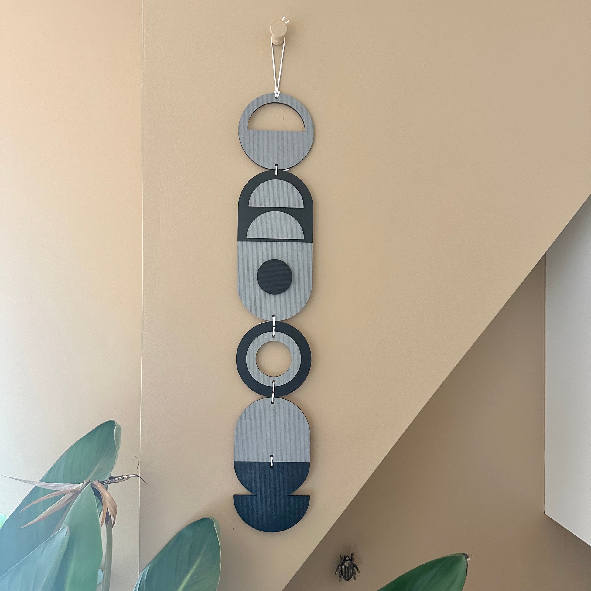 A black and grey handmade geometric wood wall hanging. In a modern Bauhaus art style. Featuring a textured effect through layer wood pieces and laser etching. Measuring 68cm in length x 10cm wide