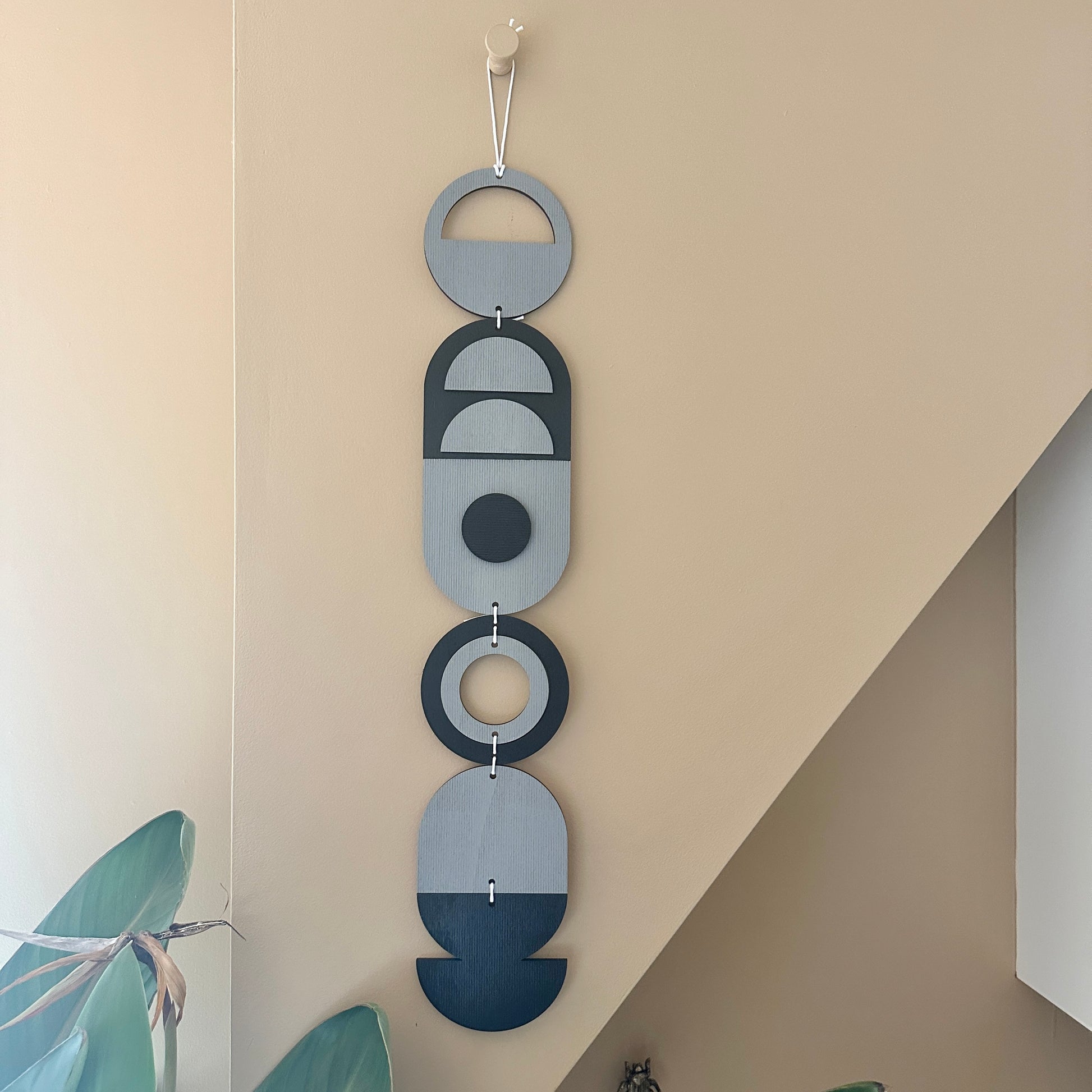 A black and grey handmade geometric wood wall hanging. In a modern Bauhaus art style. Featuring a textured effect through layer wood pieces and laser etching. Measuring 68cm in length x 10cm wide