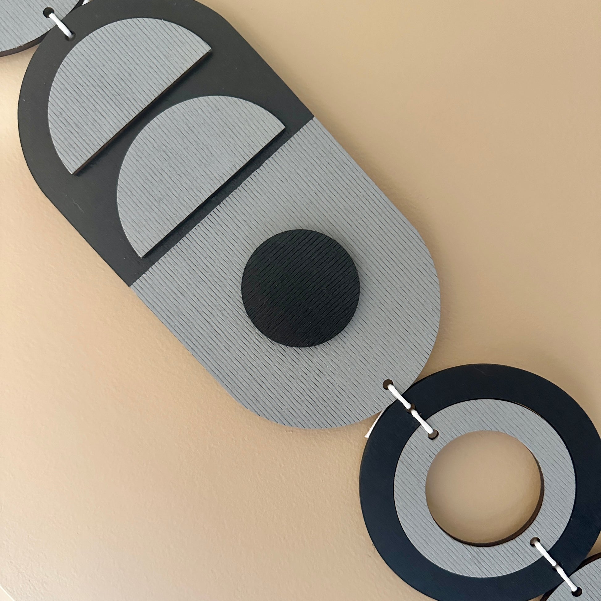 A black and grey handmade geometric wood wall hanging. In a modern Bauhaus art style. Featuring a textured effect through layer wood pieces and laser etching. Measuring 68cm in length x 10cm wide