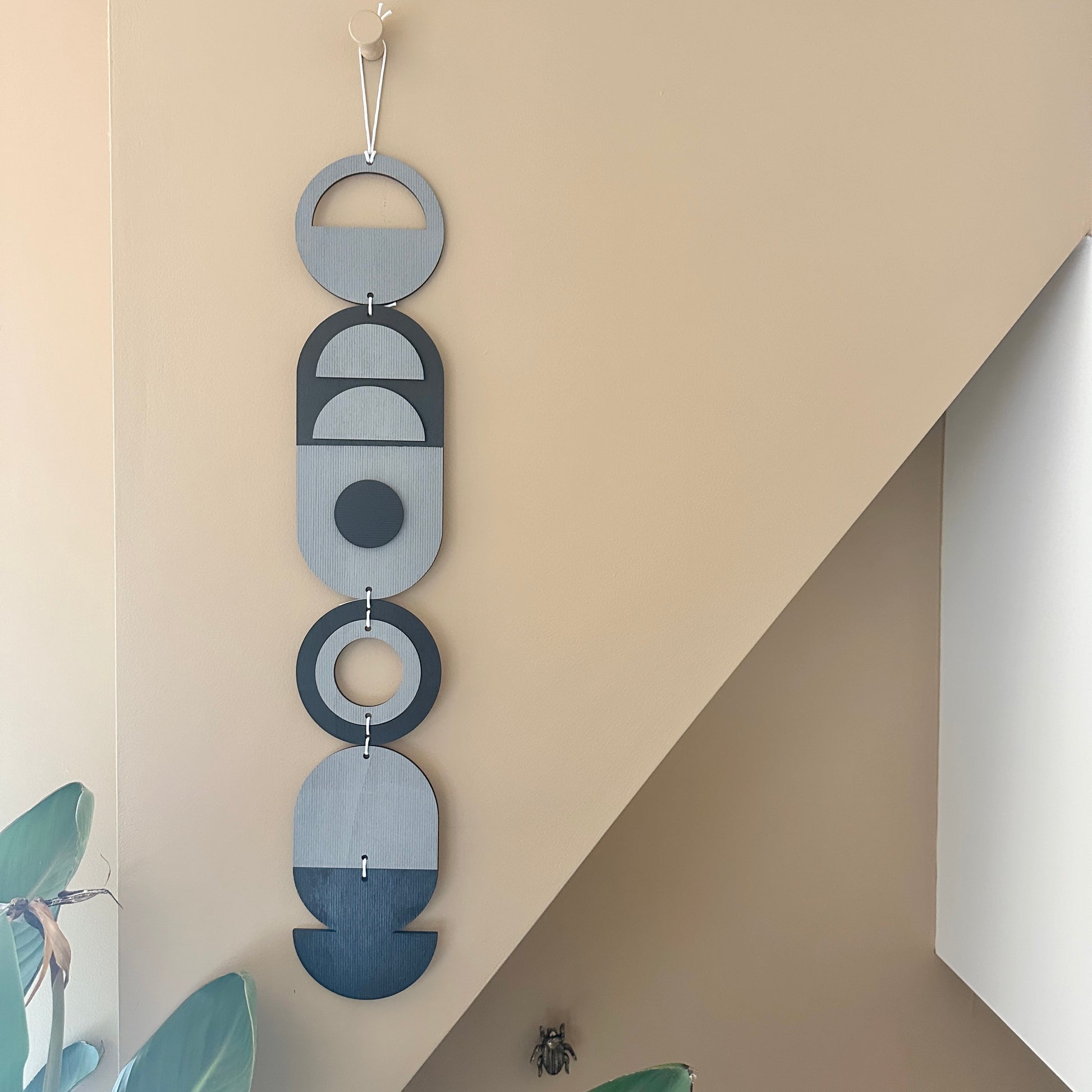 A black and grey handmade geometric wood wall hanging. In a modern Bauhaus art style. Featuring a textured effect through layer wood pieces and laser etching. Measuring 68cm in length x 10cm wide