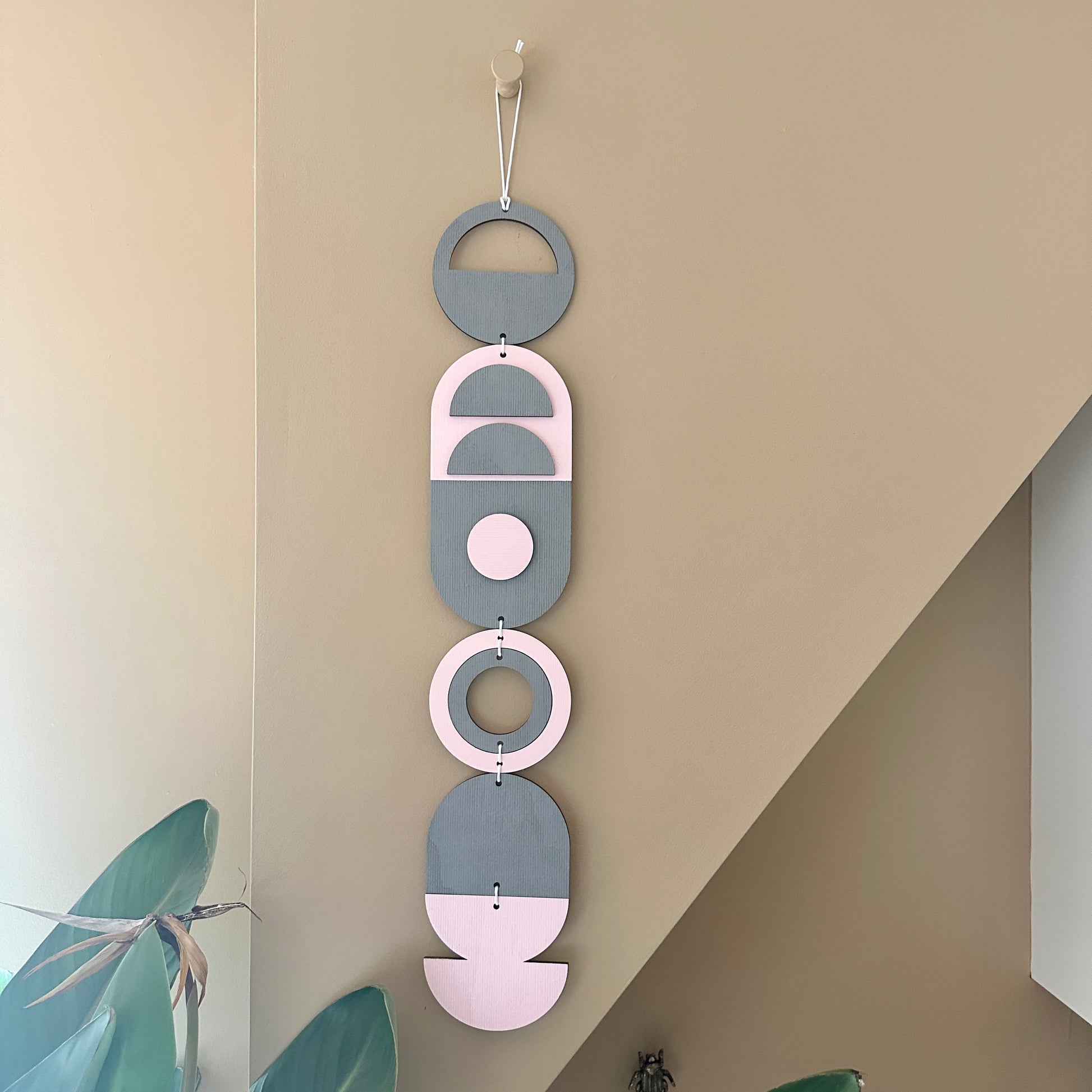 A vibrant pink and grey handmade geometric wood wall hanging. Featuring a textured effect through layer wood pieces and laser etching. Measuring 68cm in length x 10cm wide