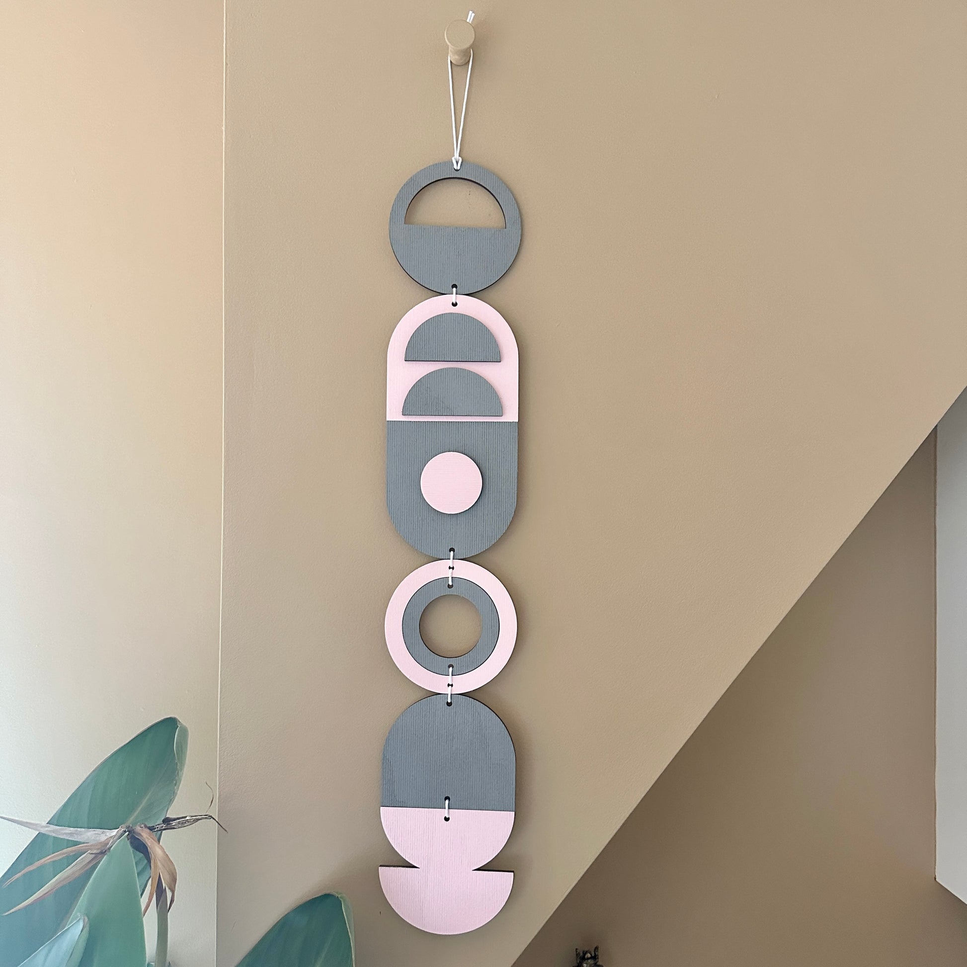 A vibrant pink and grey handmade geometric wood wall hanging. Featuring a textured effect through layer wood pieces and laser etching. Measuring 68cm in length x 10cm wide