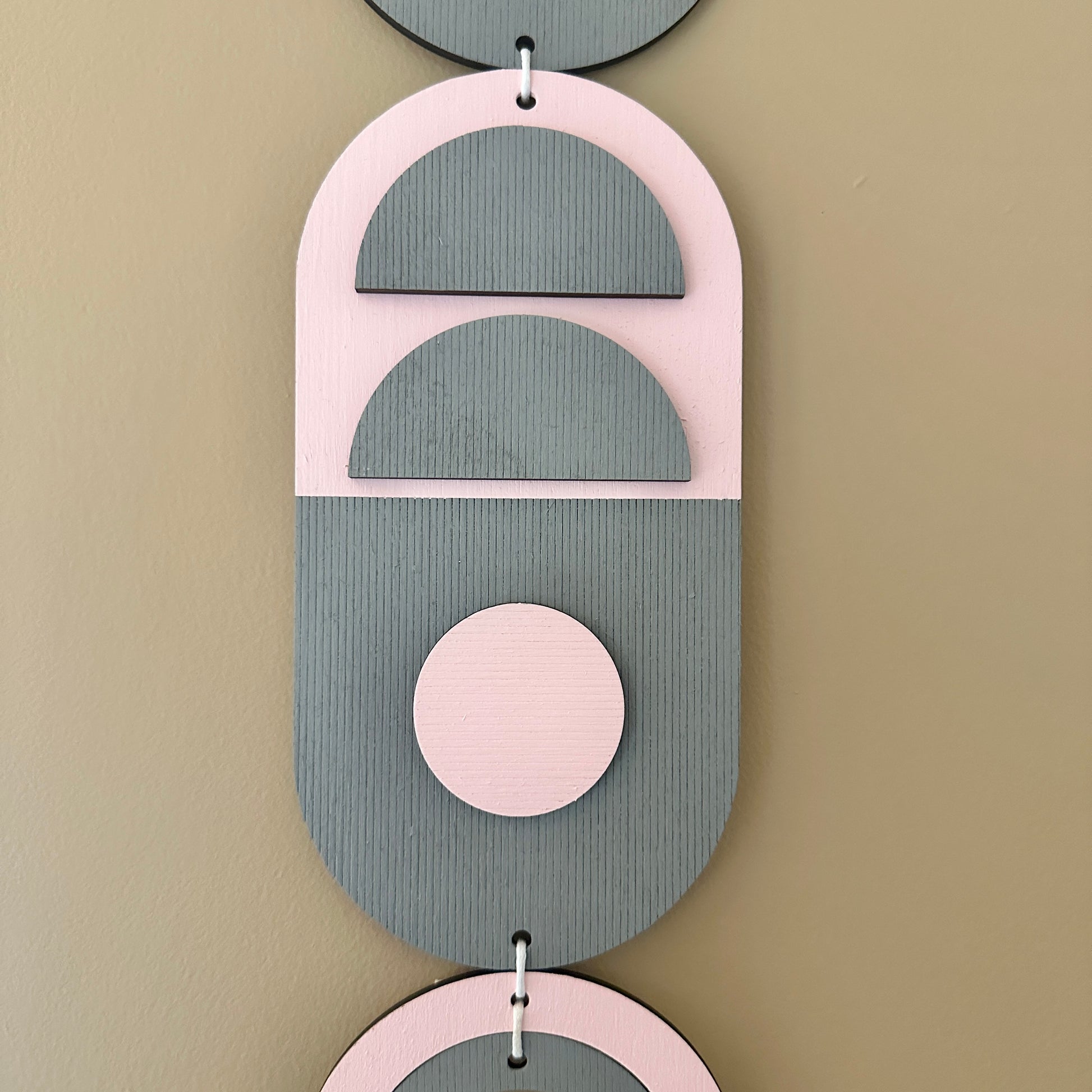 A vibrant pink and grey handmade geometric wood wall hanging. Featuring a textured effect through layer wood pieces and laser etching. Measuring 68cm in length x 10cm wide
