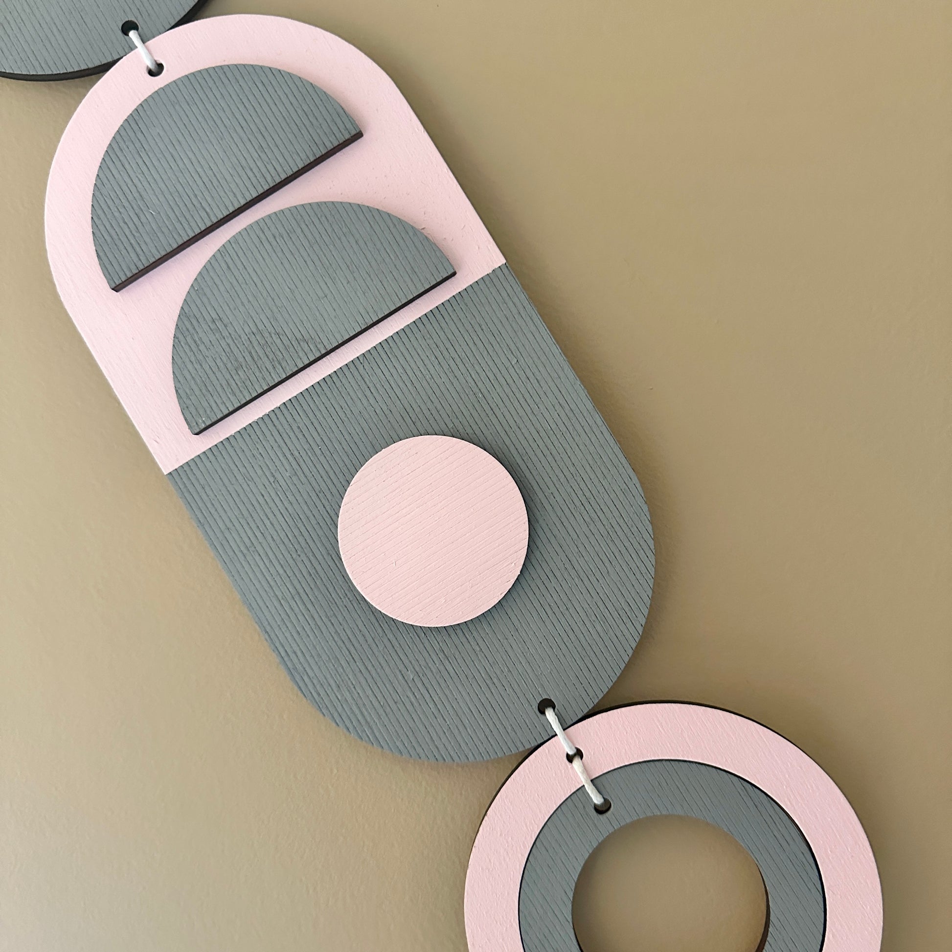 A vibrant pink and grey handmade geometric wood wall hanging. Featuring a textured effect through layer wood pieces and laser etching. Measuring 68cm in length x 10cm wide