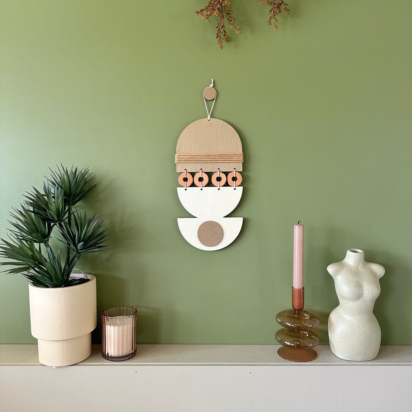 A bohemian style geometric wall hanging made from plywood part painted in beige and part left wood. Cut in semi circles and circles. With terracotta ceramic discs and brown yarn to add texture to the piece. 40cmL x 16cmW