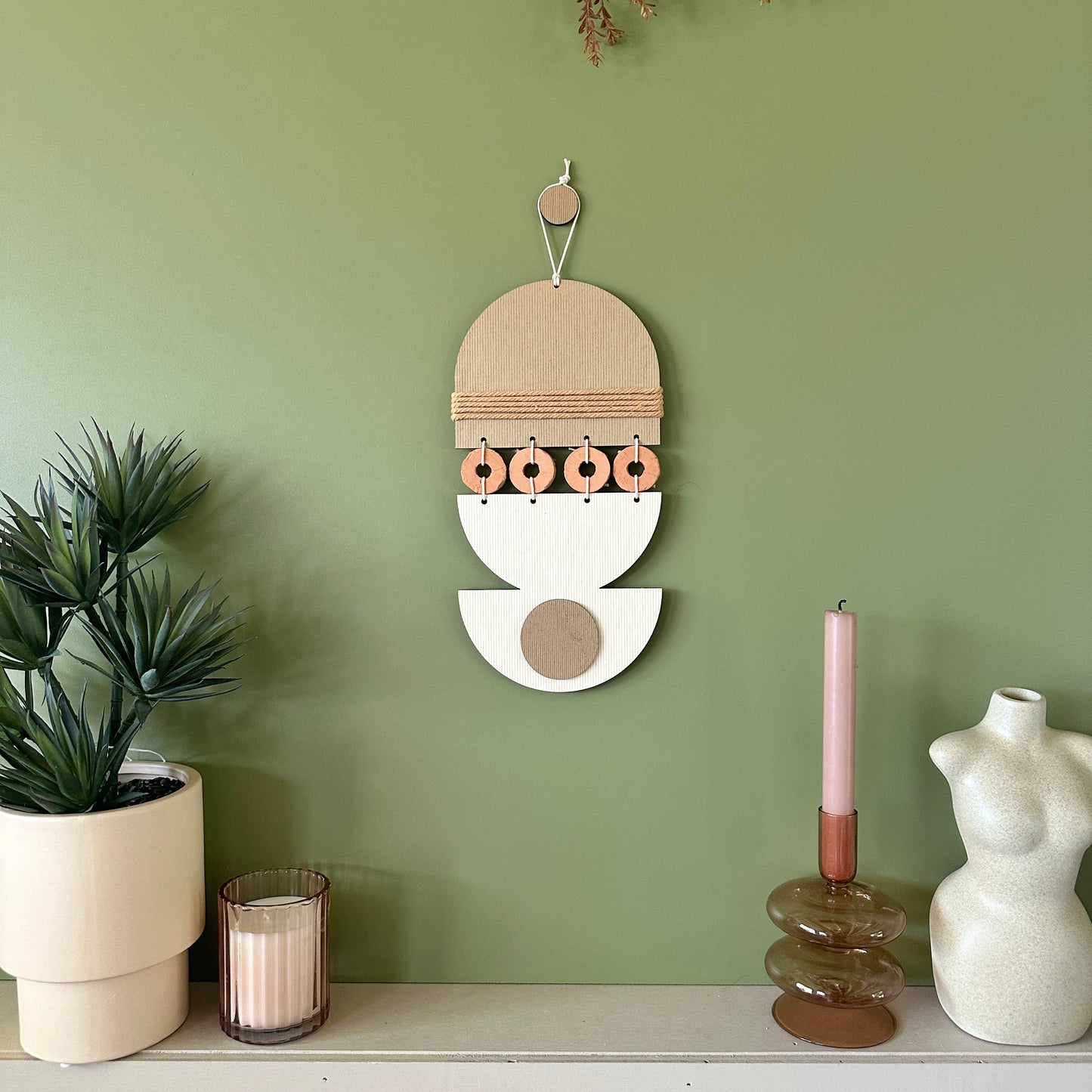 A bohemian style geometric wall hanging made from plywood part painted in beige and part left wood. Cut in semi circles and circles. With terracotta ceramic discs and brown yarn to add texture to the piece. 40cmL x 16cmW