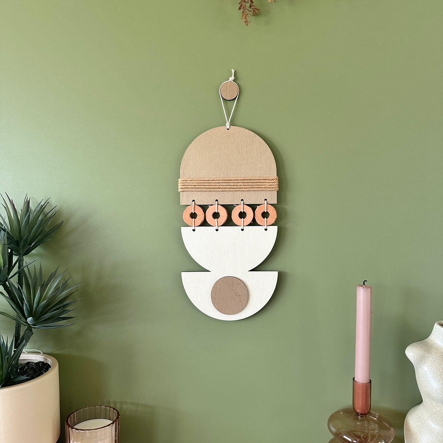 A bohemian style geometric wall hanging made from plywood part painted in beige and part left wood. Cut in semi circles and circles. With terracotta ceramic discs and brown yarn to add texture to the piece. 40cmL x 16cmW