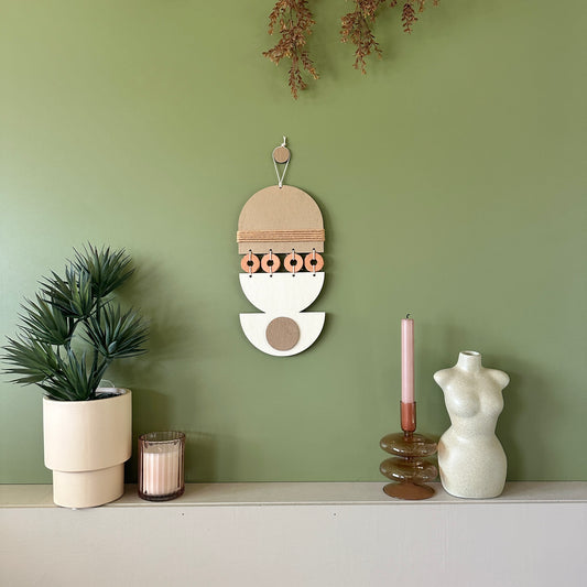 A bohemian style geometric wall hanging made from plywood part painted in beige and part left wood. Cut in semi circles and circles. With terracotta ceramic discs and brown yarn to add texture to the piece. 40cmL x 16cmW