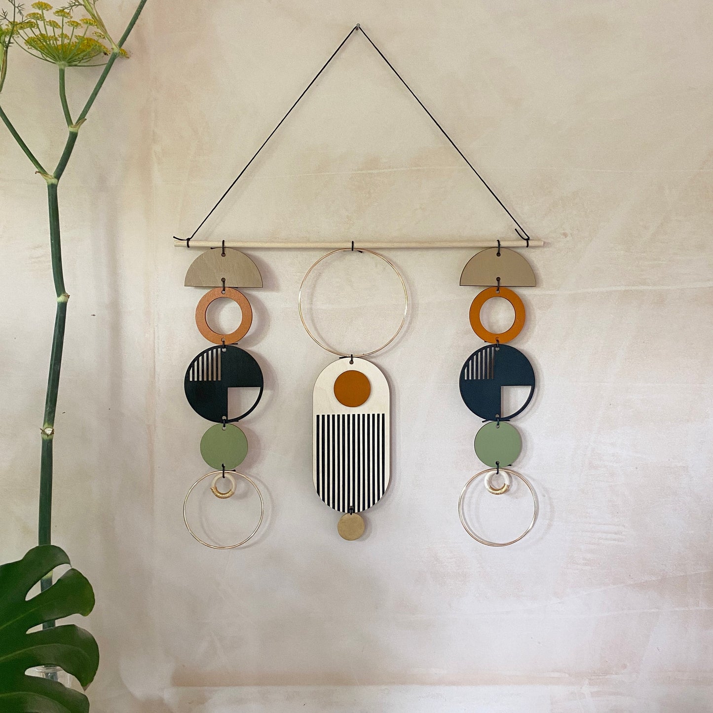 A wall hanging in a mid century modern style. Made from geometric plywood shapes painted in orange, green and black with gold metal coloured accents. Measuring - 66cm (26”) long, 32cm (13”) wide.