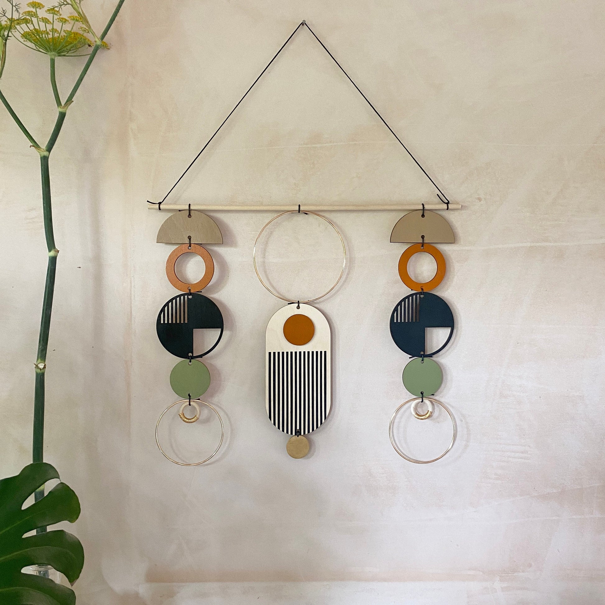 A wall hanging in a mid century modern style. Made from geometric plywood shapes painted in orange, green and black with gold metal coloured accents. Measuring - 66cm (26”) long, 32cm (13”) wide.