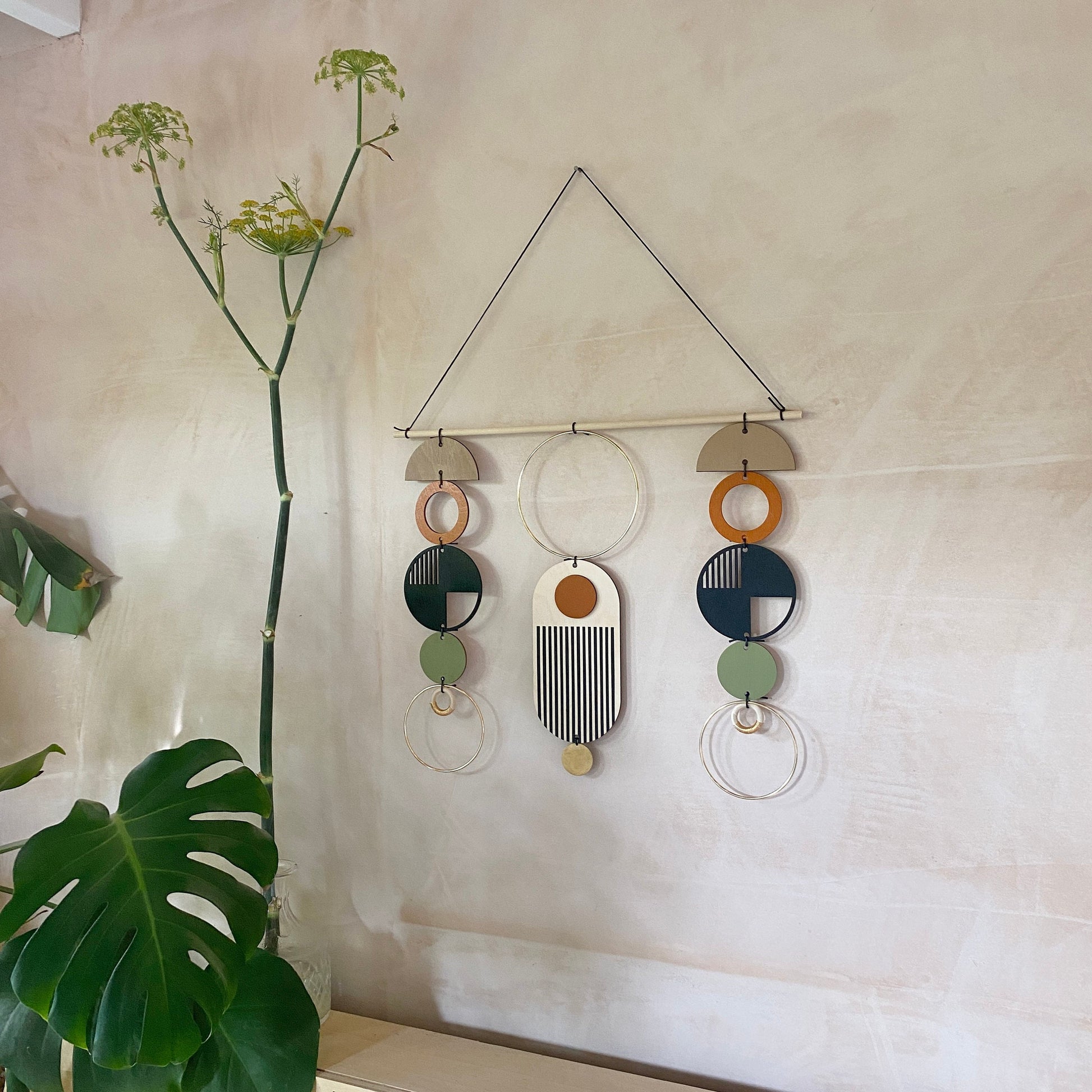 A wall hanging in a mid century modern style. Made from geometric plywood shapes painted in orange, green and black with gold metal coloured accents. Measuring - 66cm (26”) long, 32cm (13”) wide.