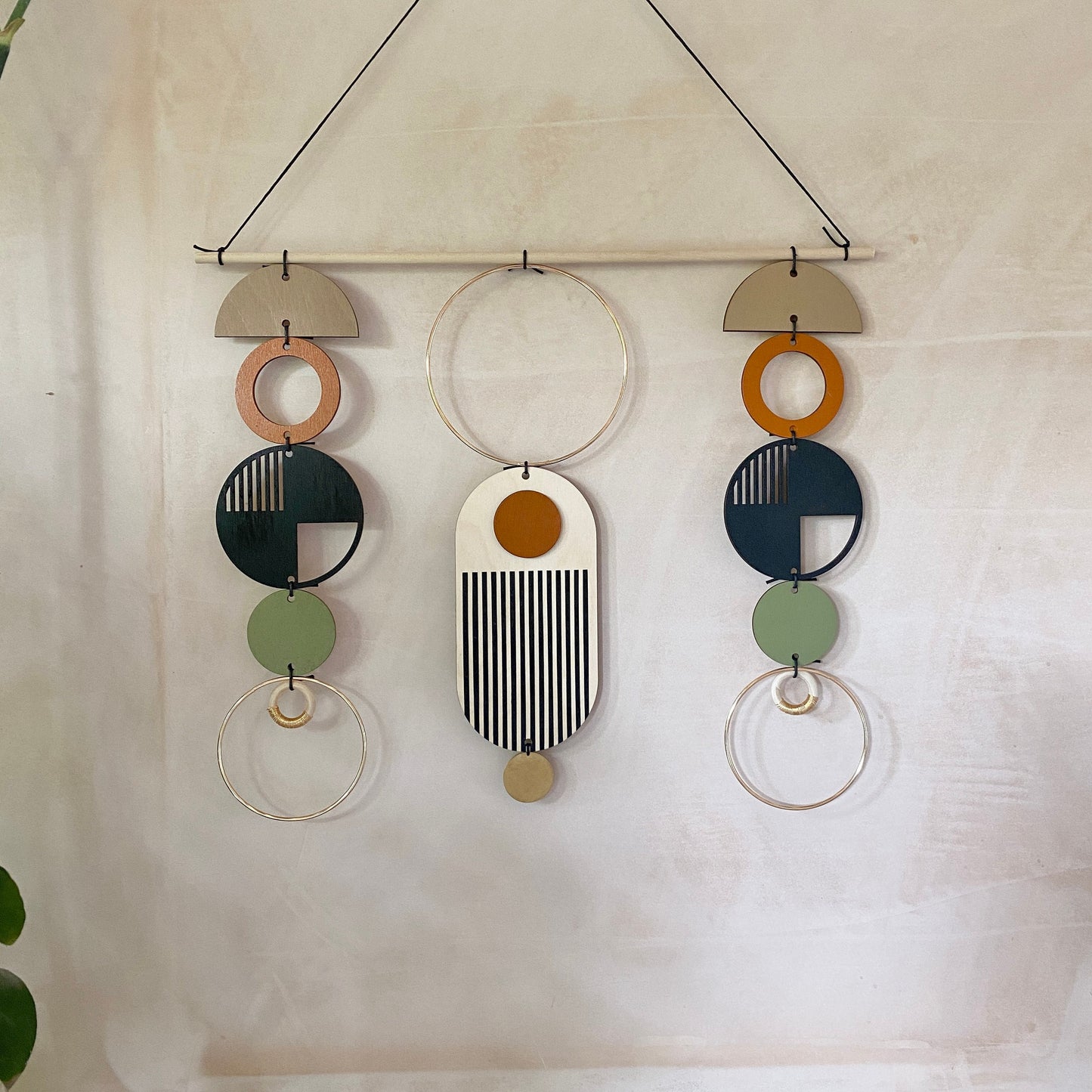 A wall hanging in a mid century modern style. Made from geometric plywood shapes painted in orange, green and black with gold metal coloured accents. Measuring - 66cm (26”) long, 32cm (13”) wide.