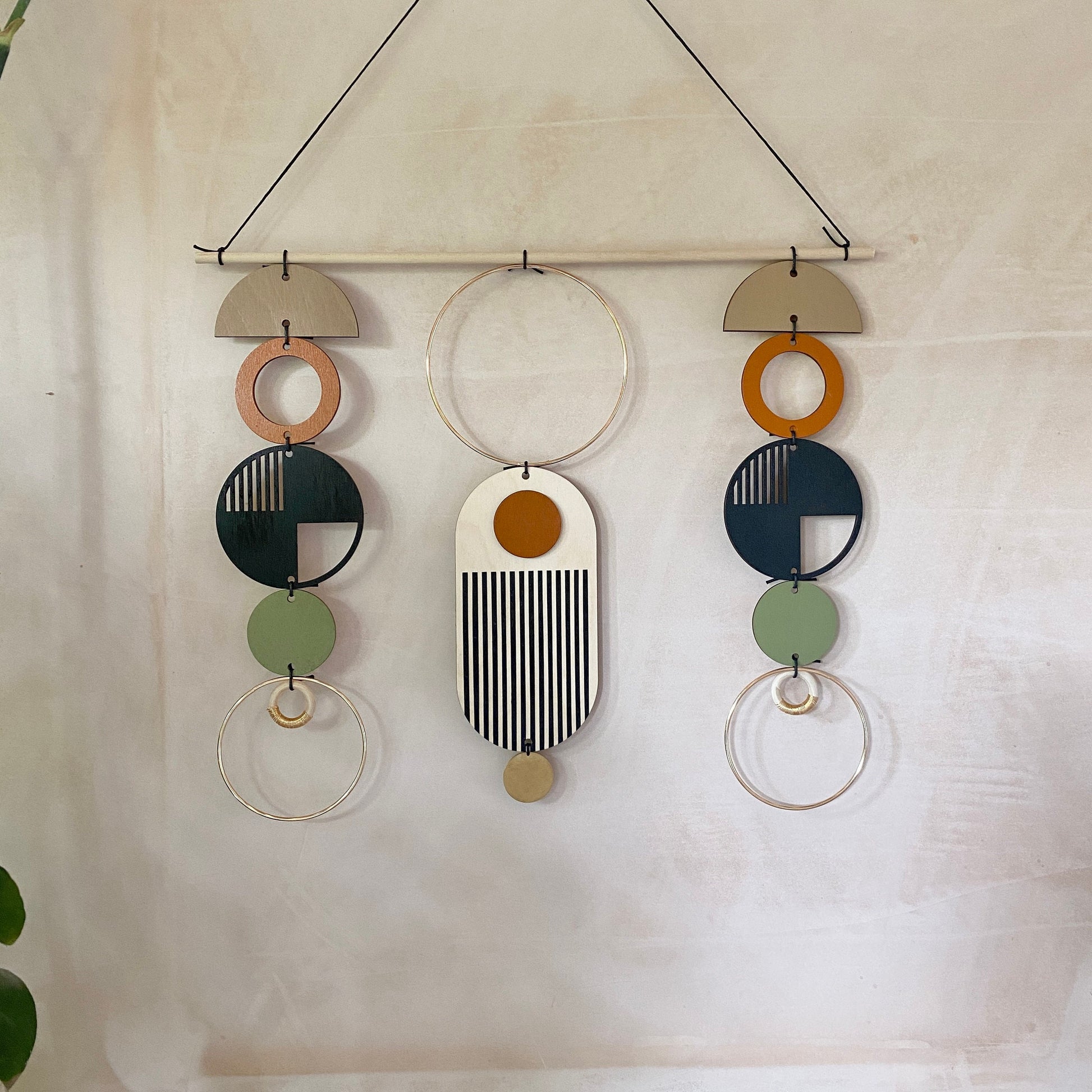 A wall hanging in a mid century modern style. Made from geometric plywood shapes painted in orange, green and black with gold metal coloured accents. Measuring - 66cm (26”) long, 32cm (13”) wide.