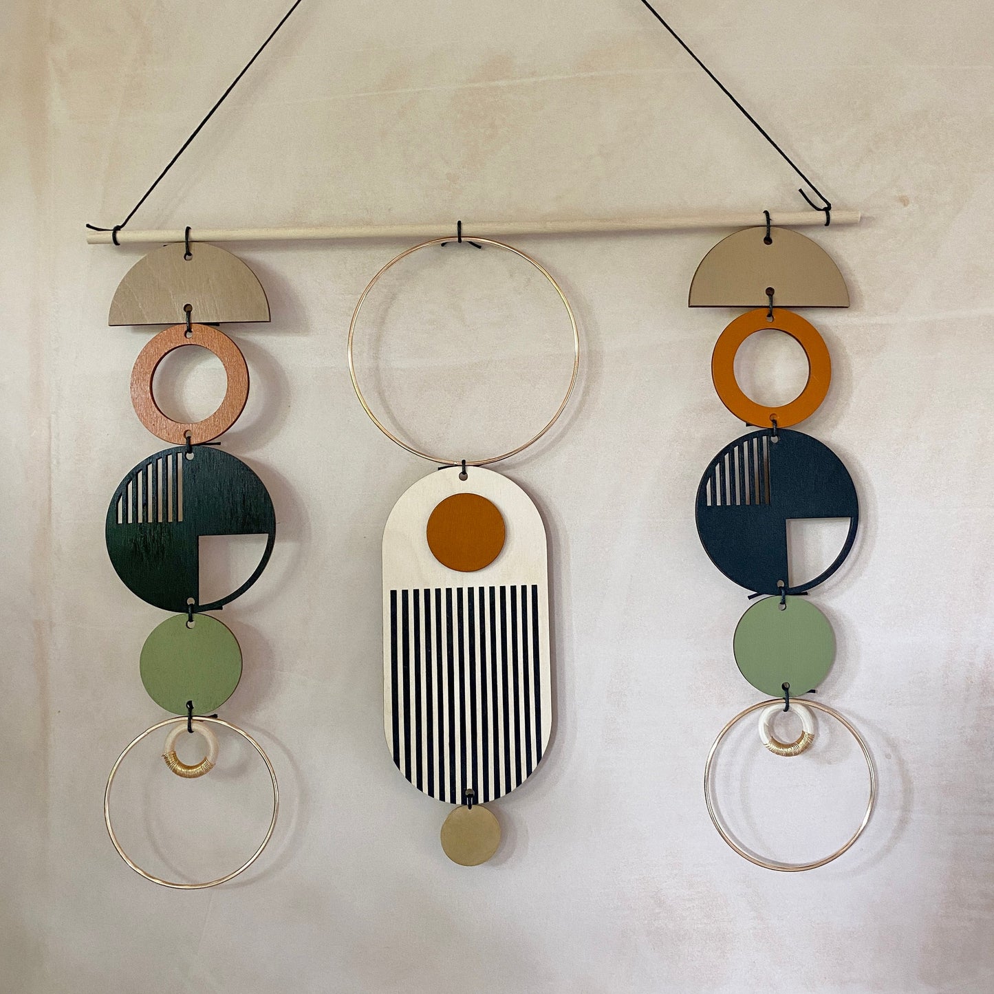 A wall hanging in a mid century modern style. Made from geometric plywood shapes painted in orange, green and black with gold metal coloured accents. Measuring - 66cm (26”) long, 32cm (13”) wide.