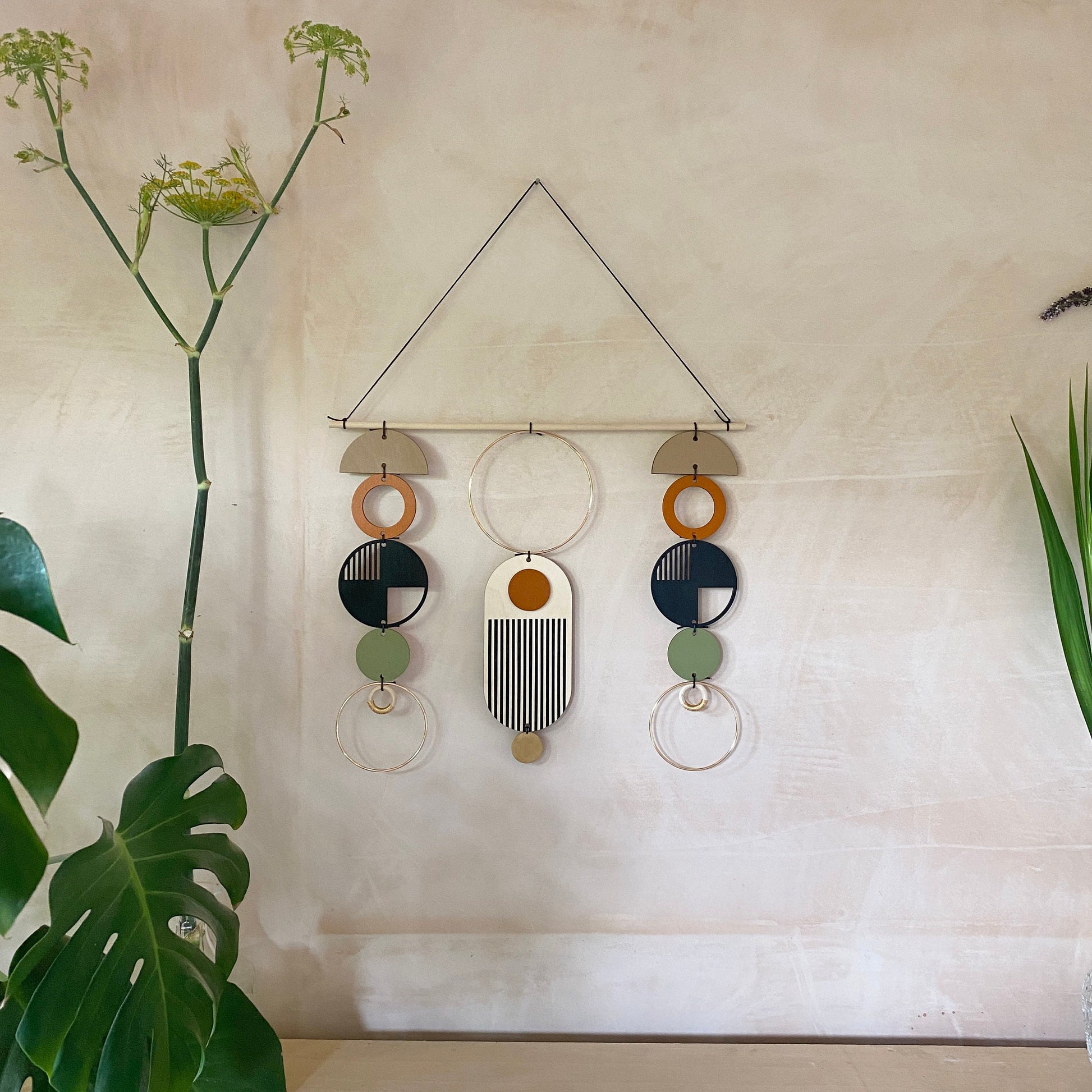 A wall hanging in a mid century modern style. Made from geometric plywood shapes painted in orange, green and black with gold metal coloured accents. Measuring - 66cm (26”) long, 32cm (13”) wide.