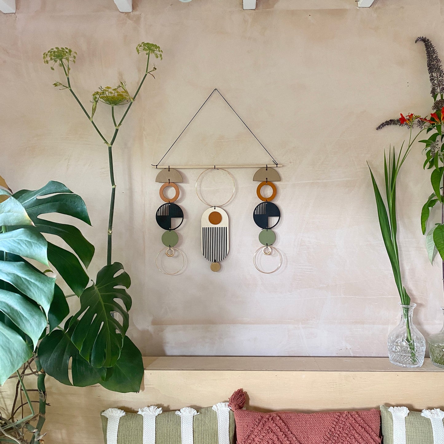 A wall hanging in a mid century modern style. Made from geometric plywood shapes painted in orange, green and black with gold metal coloured accents. Measuring - 66cm (26”) long, 32cm (13”) wide.