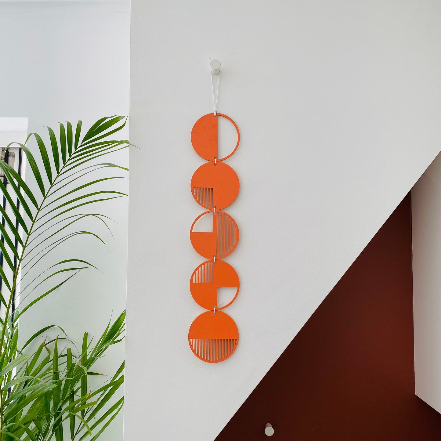 Orange wall art made from 5 wood discs tied in a single row. With laser cut geometric patterns.