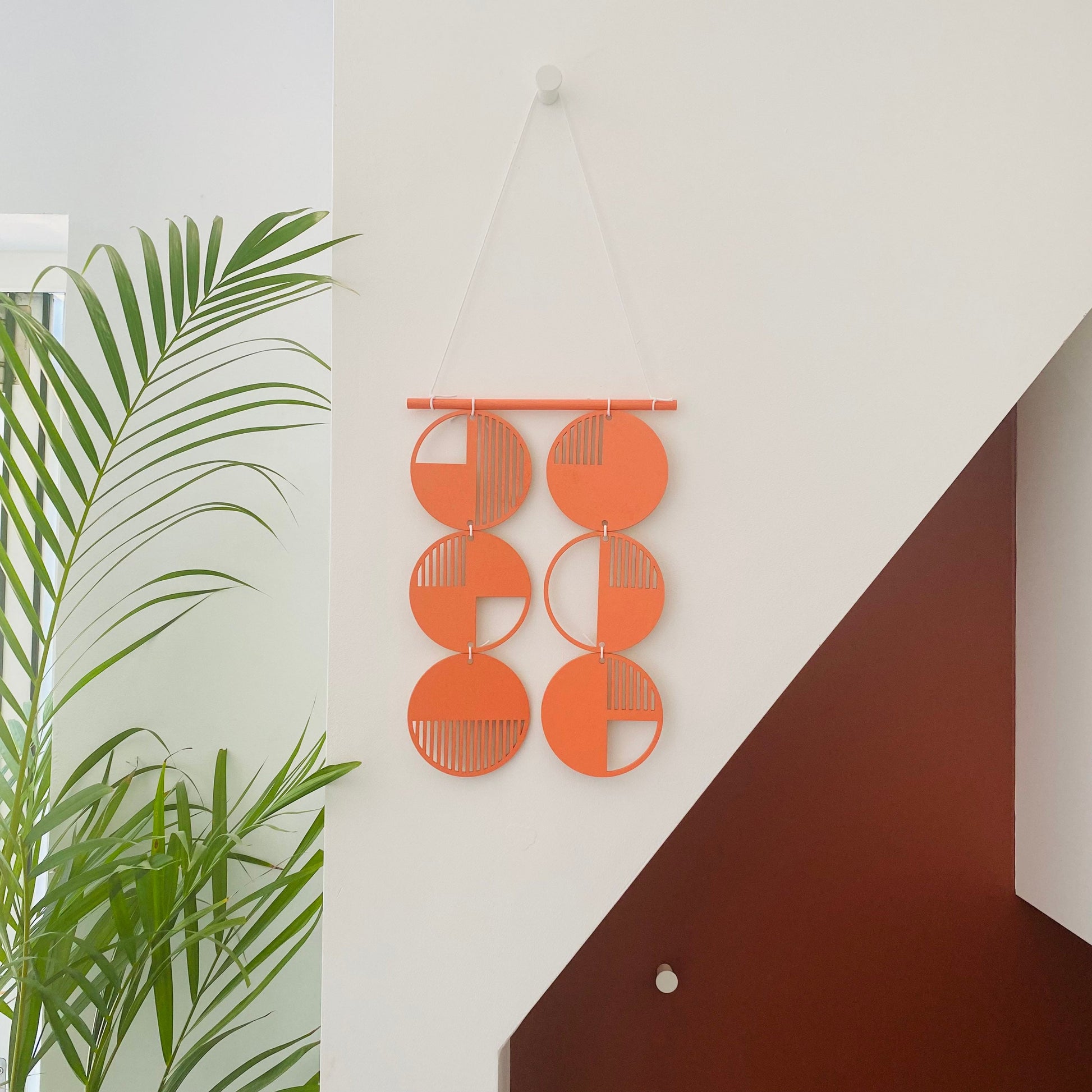 Orange wall art made from 6 wood discs tied to each other 2 rows of 3. With laser cut geometric patterns.