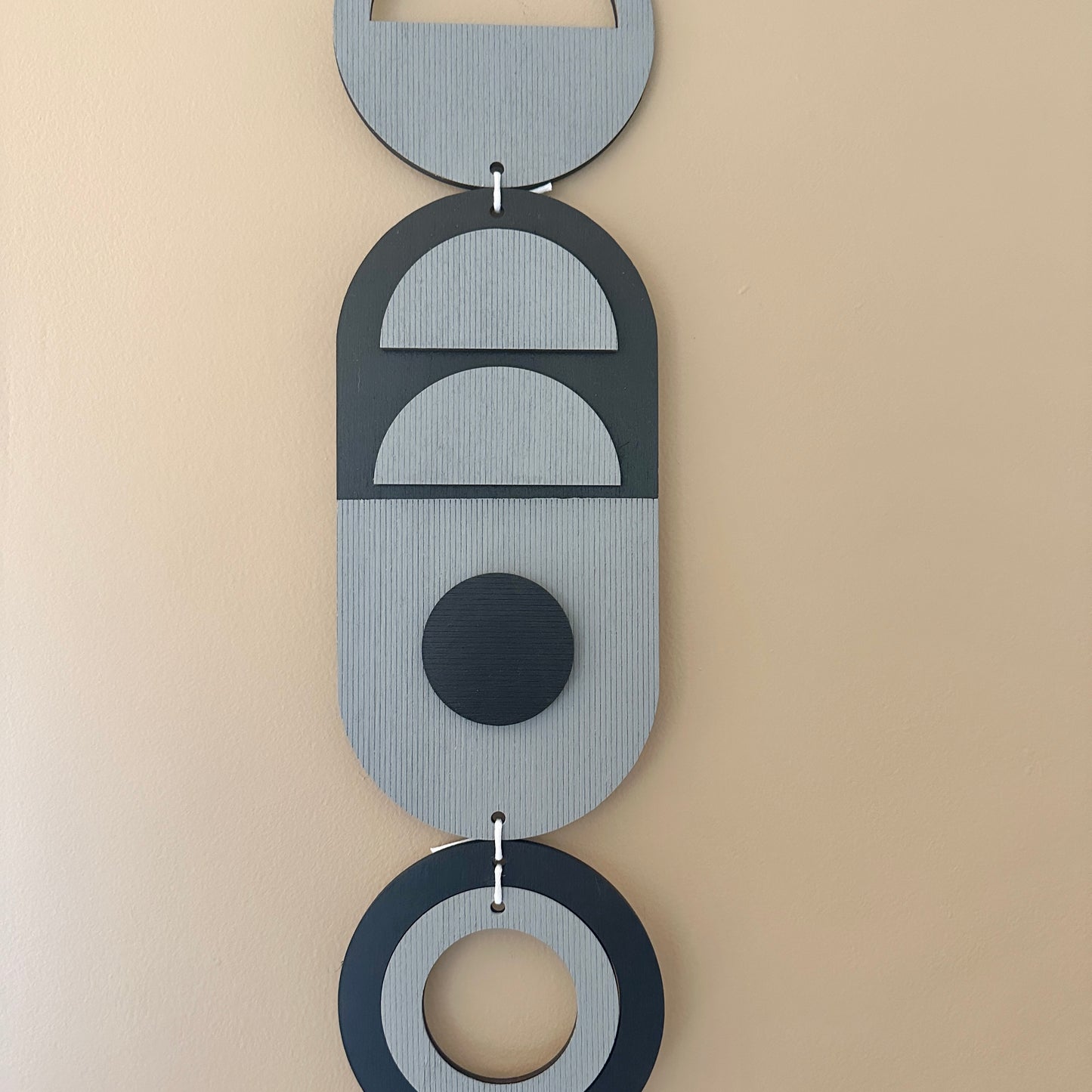 A black and grey handmade geometric wood wall hanging. In a modern Bauhaus art style. Featuring a textured effect through layer wood pieces and laser etching. Measuring 68cm in length x 10cm wide