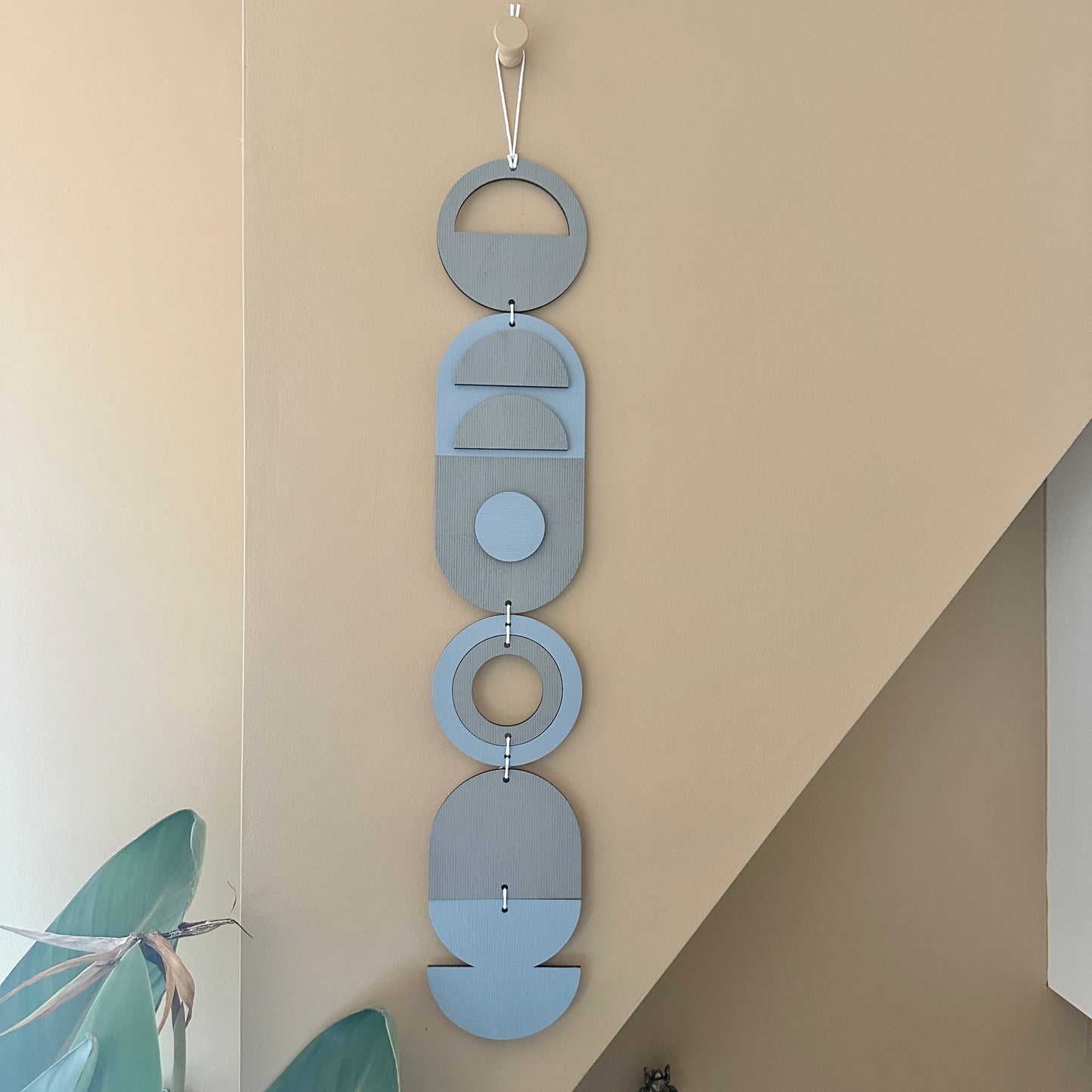 A light blue and grey handmade geometric wood wall hanging. In a modern Bauhaus art style. Featuring a textured effect through layer wood pieces and laser etching. Measuring 68cm in length x 10cm wide