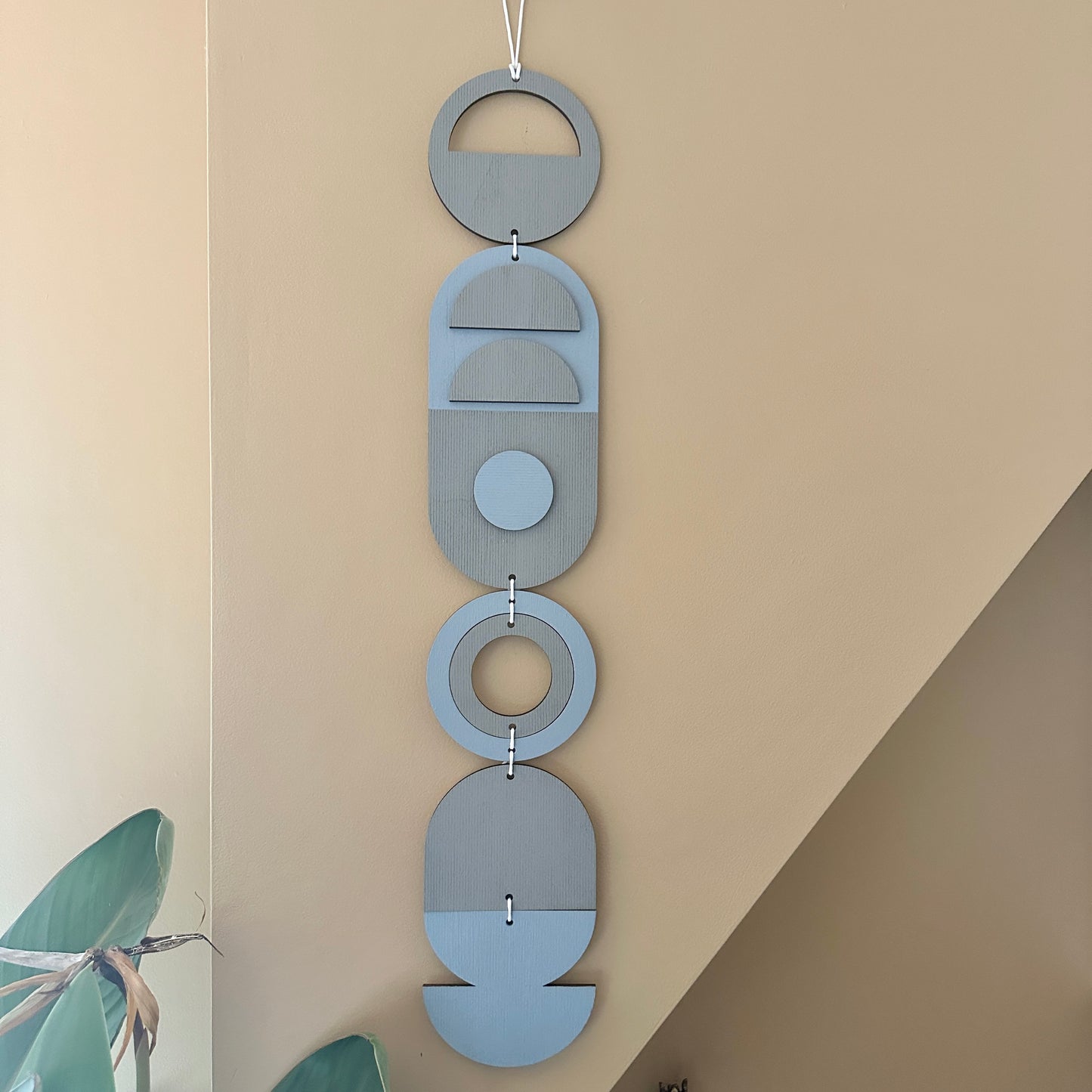 A light blue and grey handmade geometric wood wall hanging. In a modern Bauhaus art style. Featuring a textured effect through layer wood pieces and laser etching. Measuring 68cm in length x 10cm wide