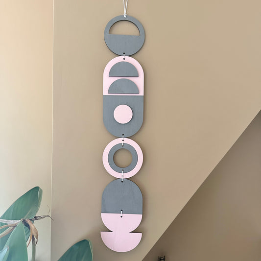 A vibrant pink and grey handmade geometric wood wall hanging. Featuring a textured effect through layer wood pieces and laser etching. Measuring 68cm in length x 10cm wide