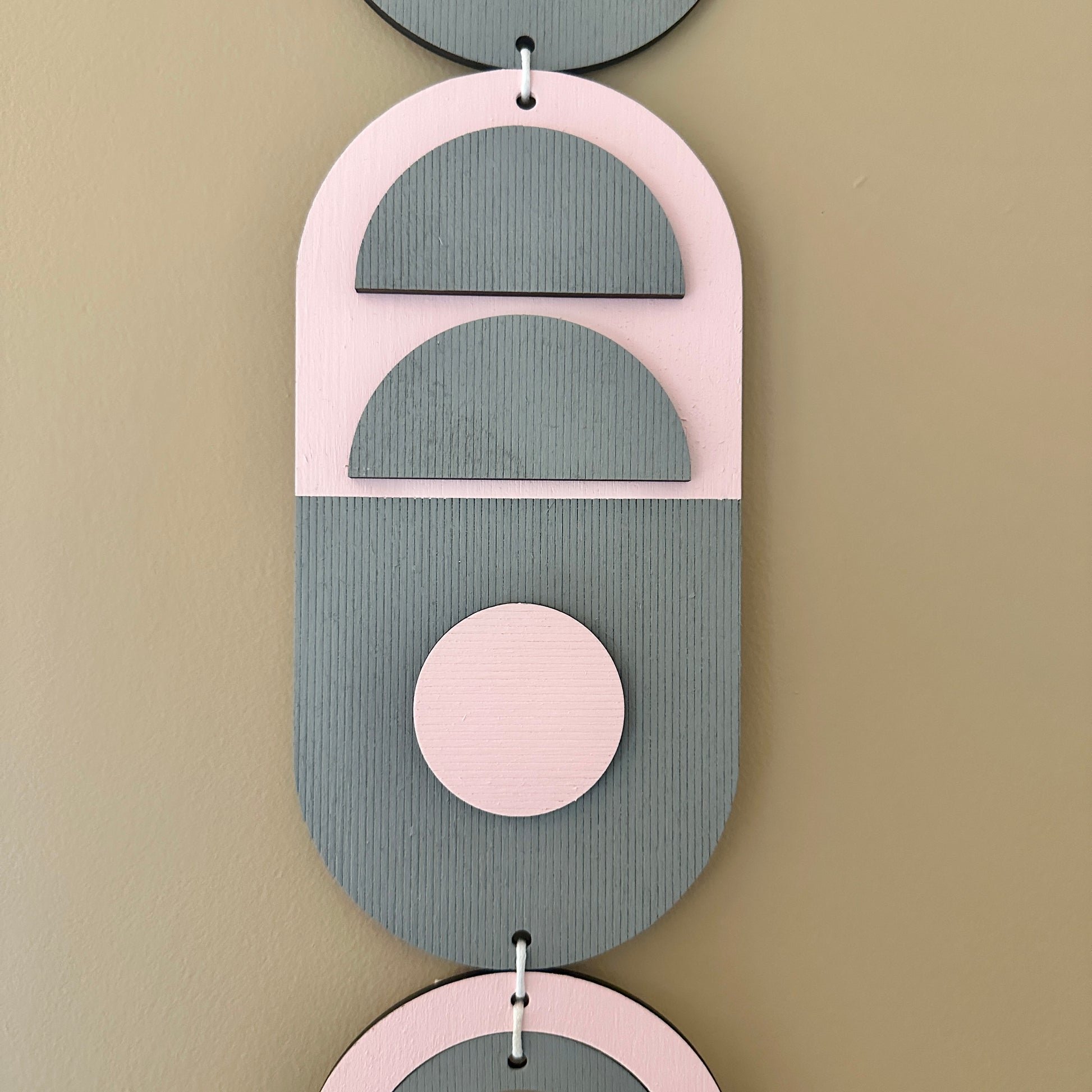 A vibrant pink and grey handmade geometric wood wall hanging. Featuring a textured effect through layer wood pieces and laser etching. Measuring 68cm in length x 10cm wide