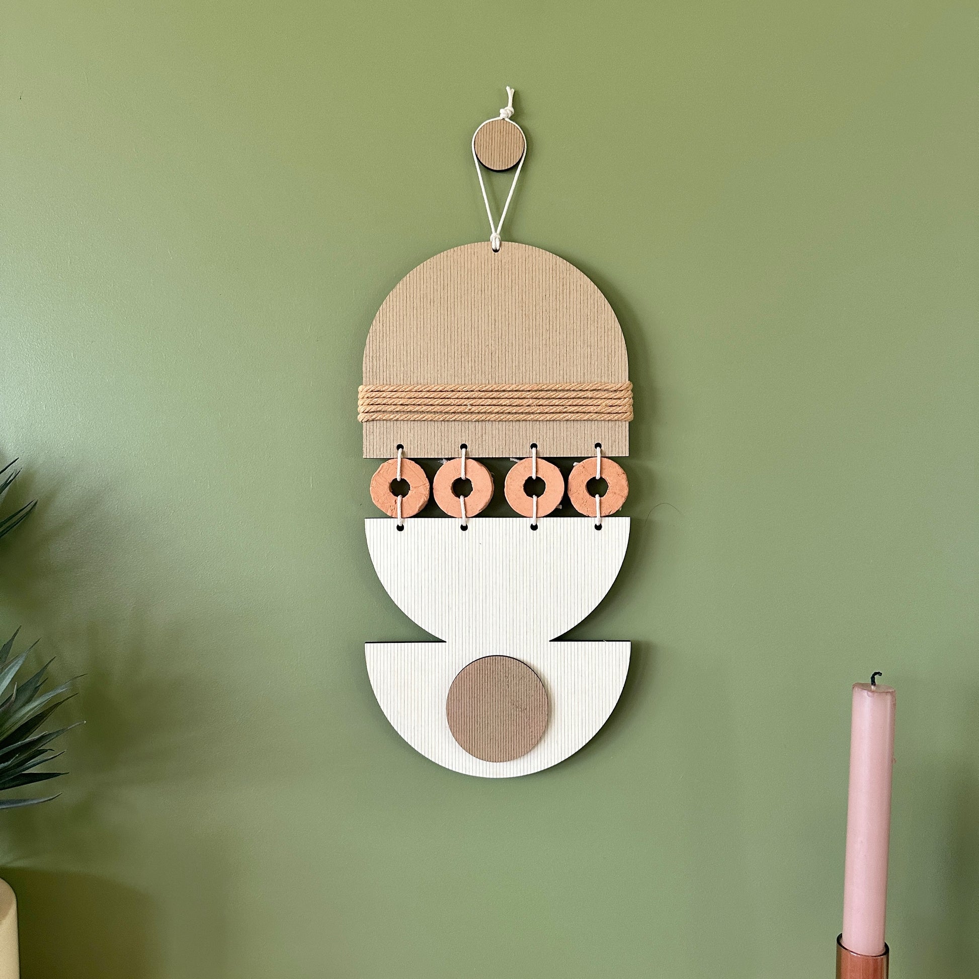 A bohemian style geometric wall hanging made from plywood part painted in beige and part left wood. Cut in semi circles and circles. With terracotta ceramic discs and brown yarn to add texture to the piece. 40cmL x 16cmW