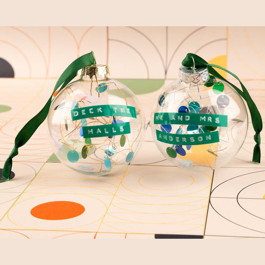 Glass baubles with green and blue sequins on silver or gold wire with a green ribbon to hang it from. With a personalised message embossed on green tape.