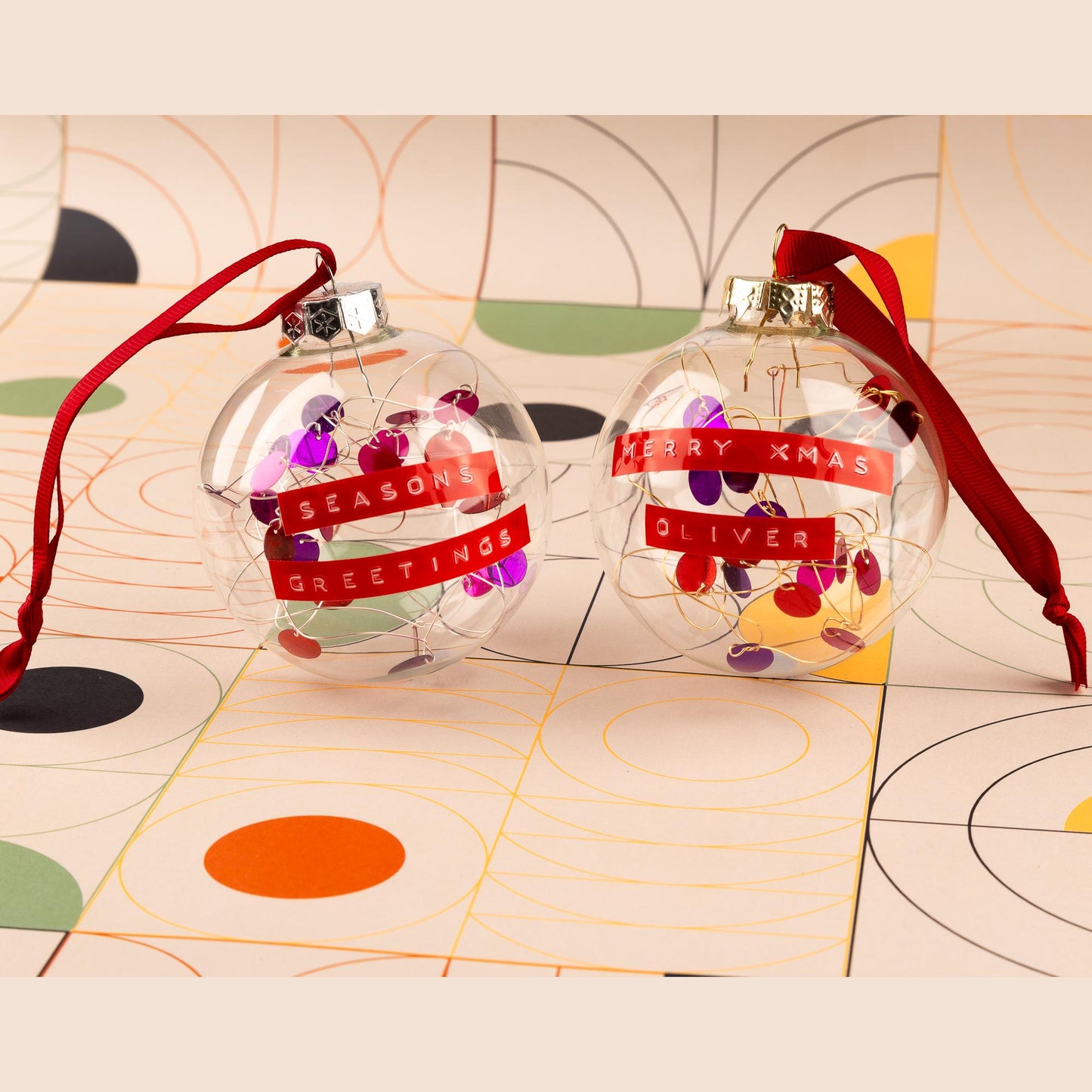 Two glass baubles with red and purple sequins on silver or gold wire with red ribbon. With a personalised message written on red tape.