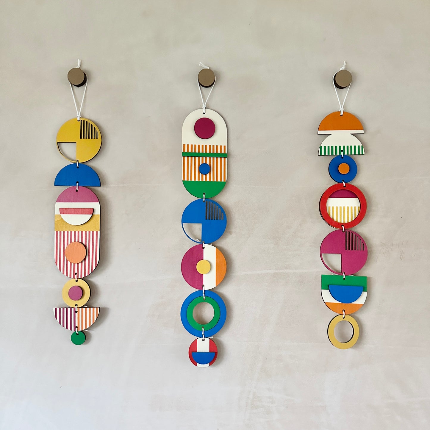 Three wall hangings in a rainbow colour palette made from wood cut in to geometric shapes. 