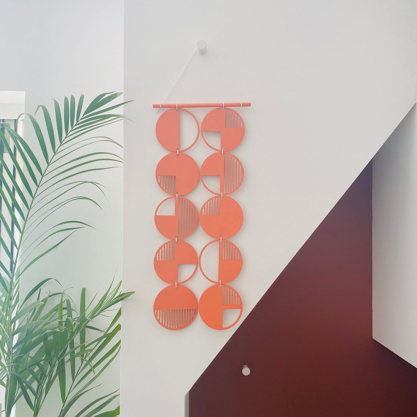 Orange wall art made from 10 wood discs tied to each other 2 rows of 5. With laser cut geometric patterns. 