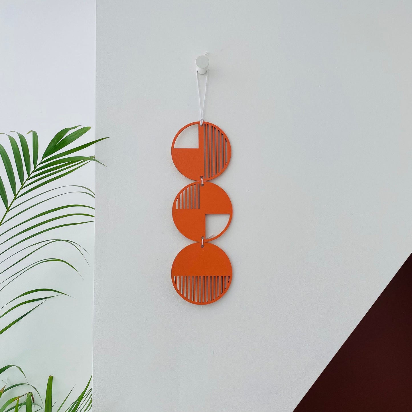 Orange wall art made from 3 wood discs tied in a column. With laser cut geometric patterns. 