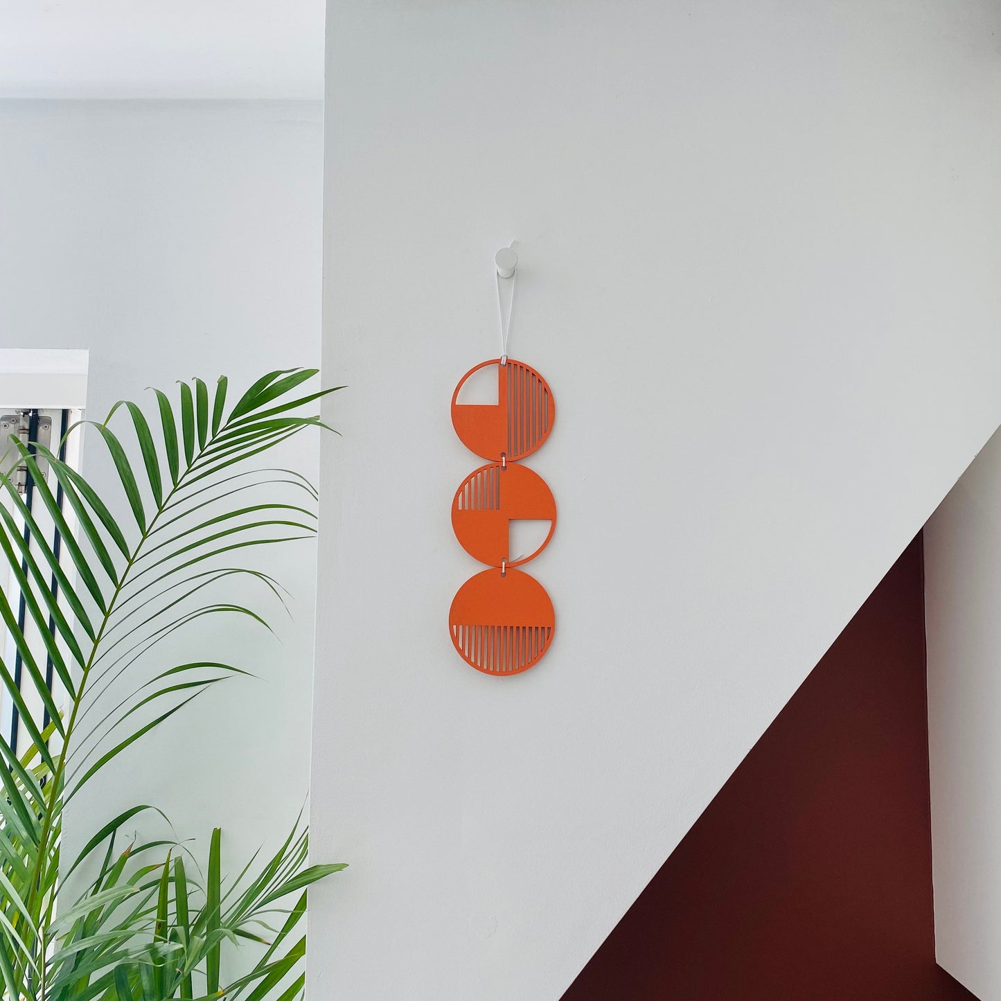 orange wall art made from 3 wood discs tied in a single column.