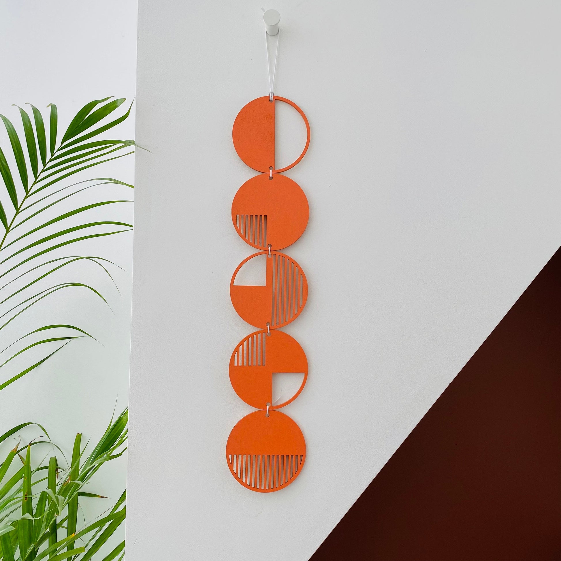 Orange wall art made from 5 wood discs tied to each other in a single row. With laser cut geometric patterns. 