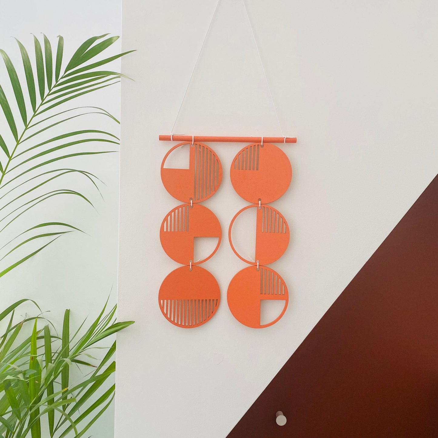 Orange wall art made from 6 wood discs tied to each other 2 rows of 3. With laser cut geometric patterns. 