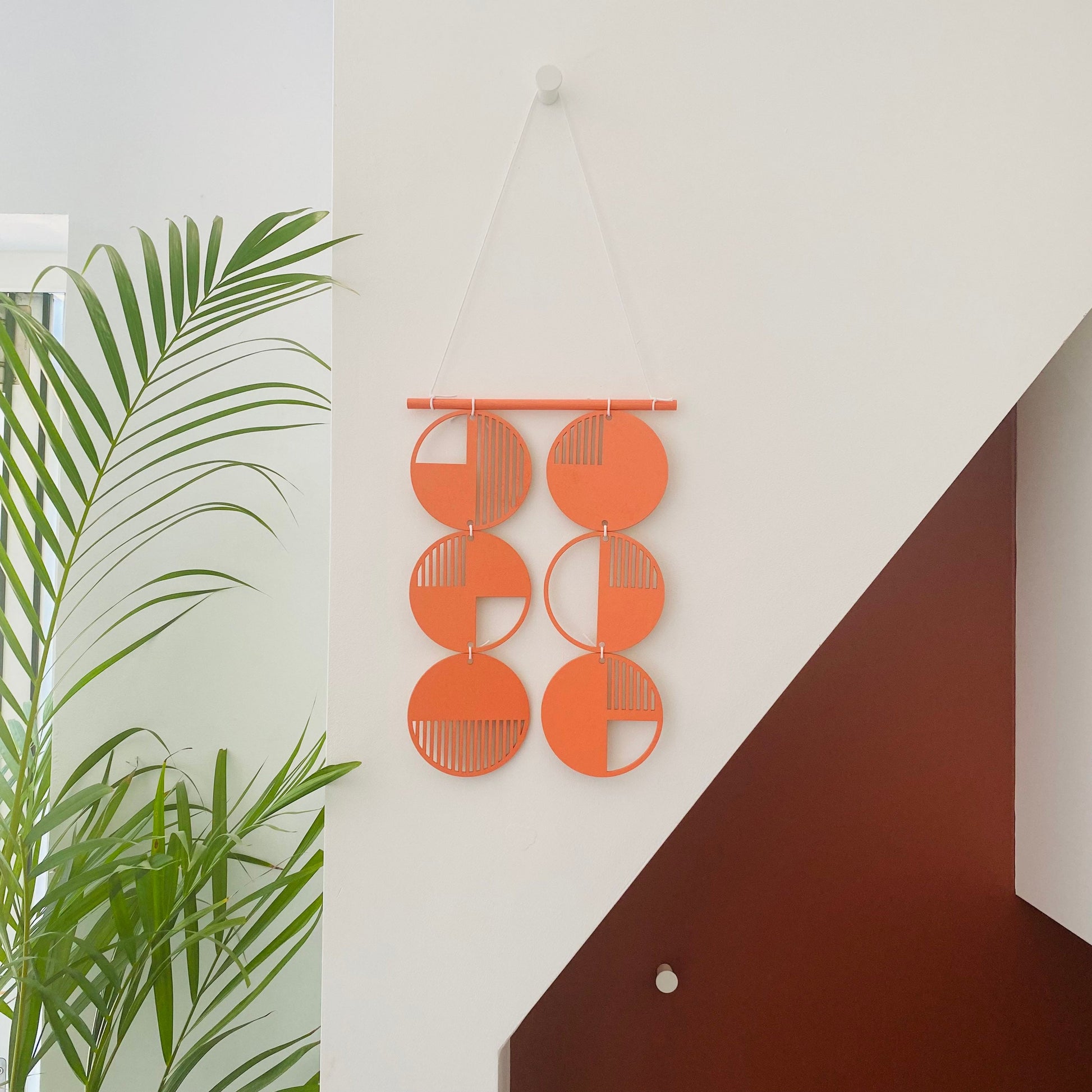 Orange wall art made from 6 wood discs tied to each other 2 rows of 3. With laser cut geometric patterns. 